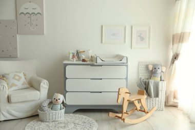 Oyuncak, koltuk ve modern değişen masalarla dolu güzel bir bebek odası.