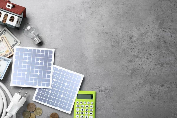 Flat lay composition with solar panels and money on grey table. Space for text