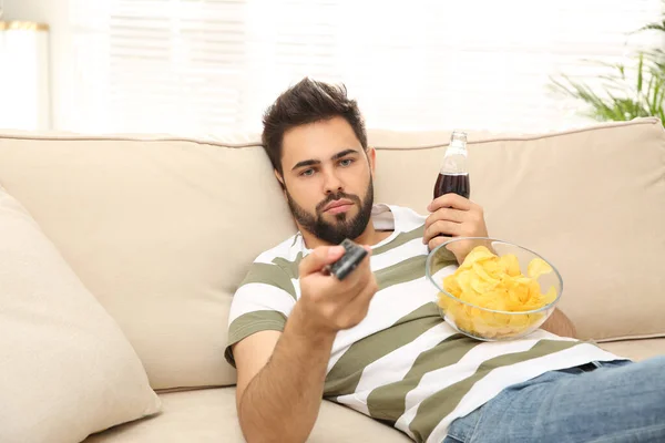 Jovem Preguiçoso Com Batatas Fritas Bebida Assistindo Sofá Casa — Fotografia de Stock