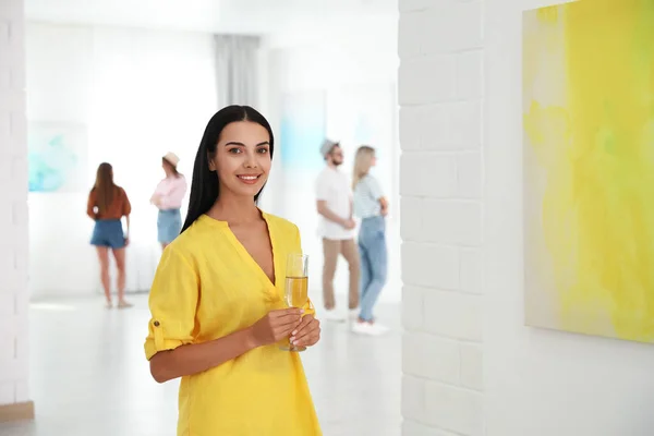 Young woman with glass of champagne at exhibition in art gallery