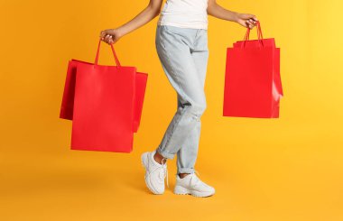 Sarı arka planda kağıt alışveriş torbaları olan genç bir kadın, yakın plan.