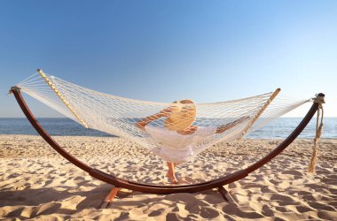 Genç bir kadın plajda hamakta dinleniyor.