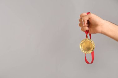 Gri arka planda altın madalya taşıyan adam, yakın plan. Tasarım için boşluk