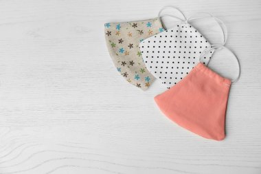 Beyaz ahşap arka planda el yapımı kumaş maskeler, metin için yeri olan düz bir yer. COVID-19 salgını sırasında kişisel koruma ekipmanları