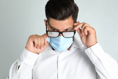 Hafif arka planda tıbbi maske takan bir adam sisli camları siliyor.
