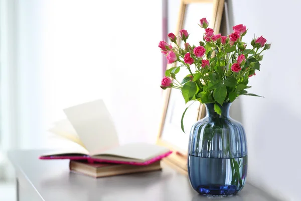 Glass vase with fresh flowers and books on grey table