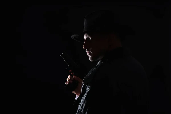 Old fashioned detective with gun on dark background. Space for text