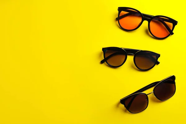 Many stylish sunglasses on yellow background, flat lay. Space for text