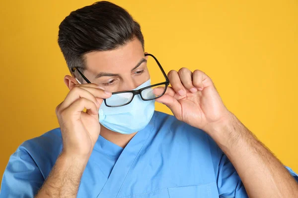 Доктор Вытирает Туманные Очки Вызванные Ношением Медицинской Маски Желтом Фоне — стоковое фото