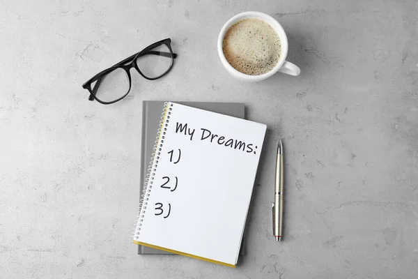 Notebook with dreams list on grey table, flat lay