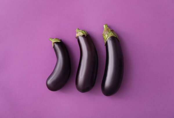 Raw ripe eggplants on purple background, flat lay