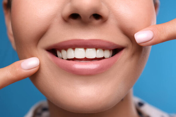 Young woman with beautiful smile on blue background, closeup. Cosmetic dentistry