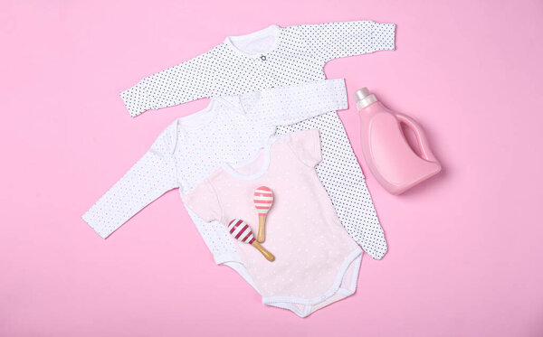 Flat lay composition with bottle of detergent and children's clothes on pink background