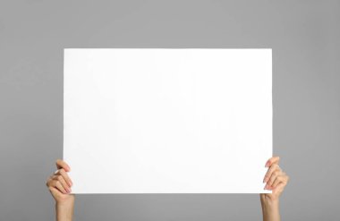 Gri arka planda beyaz boş poster tutan kadın, yakın plan. Tasarım için model