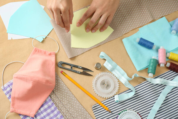 Женщина делает шаблон для шитья ткани маски за столом, крупным планом. Средства индивидуальной защиты во время пандемии COVID-19