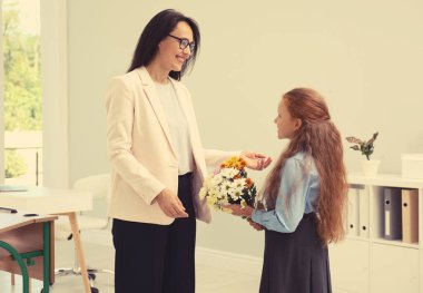 Okul kızı elinde buketle sınıftaki pedagogunu tebrik ediyor. Öğretmenler Günü