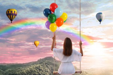 Hayal dünyası. Balonları sallanan genç bir kadın, arka planda günbatımı altında gökyüzü