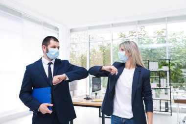 Maskeli ofis çalışanları iş yerinde dirseklerini çarpıştırarak birbirlerini selamlıyorlar.