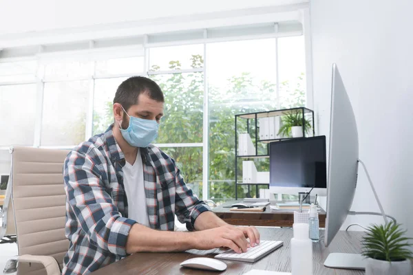 Office employee in respiratory mask at workplace