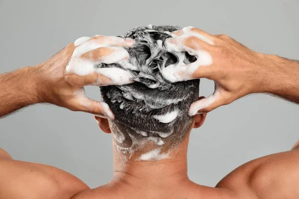 Man washing hair on grey background, back view