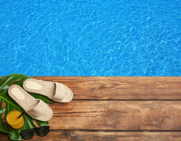 Beach accessories on wooden deck near swimming pool, flat lay. Space for text