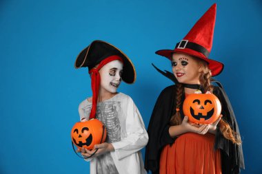 Balkabağı kovanlı şirin çocuklar mavi arka planda Cadılar Bayramı kostümleri giyiyorlar.