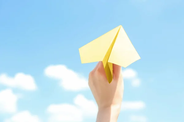 Woman holding paper plane against blue sky, closeup. Space for text