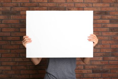 Kırmızı tuğla duvarın yanında beyaz boş poster tutan bir kadın. Tasarım için model