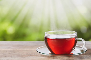 Ahşap masada, bulanık yeşil arka planda, cam bardak taze çay. Metin için boşluk