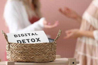 Pembe arka planda sohbet eden kadınlar, dijital detoks işaretli hasır sepete odaklanın