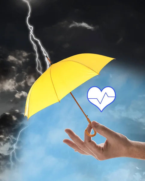 保険の概念 嵐の間 黄色の傘で心臓のイラストをカバーする男 クローズアップ — ストック写真