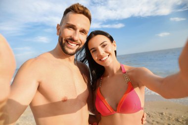 Mutlu genç çift sahilde selfie çekiyor.