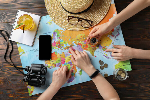 People with world map and accessories at table, top view. Travel during summer vacation