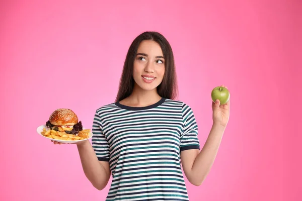 女性はピンクの背景にフランス語のフライドポテトとリンゴとバーガーの間で選択 — ストック写真