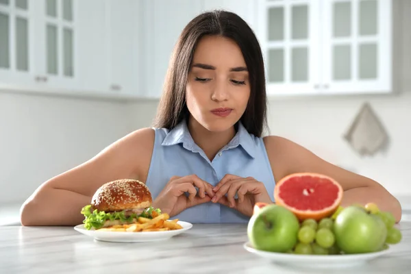 Kobieta Wybierająca Między Owocami Hamburgerem Frytkami Kuchni — Zdjęcie stockowe