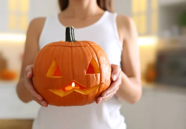 Woman holding pumpkin jack o\'lantern indoors, closeup. Halloween celebration