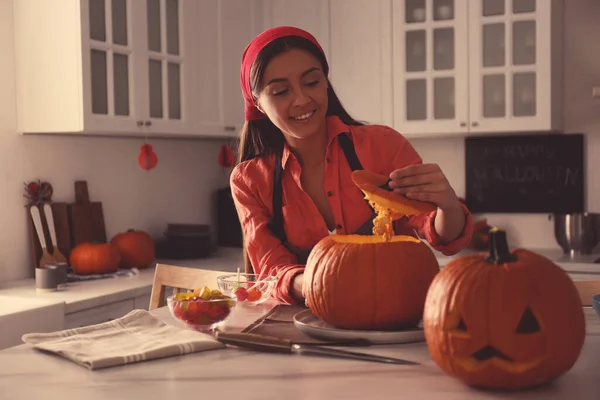 Woman making pumpkin jack o\'lantern at table in kitchen. Halloween celebration