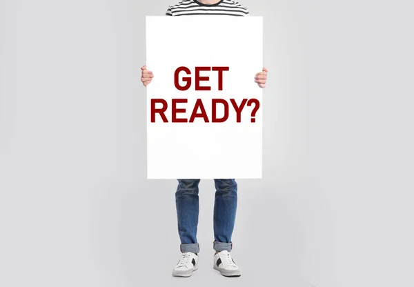 Man holding poster with text Get Ready? on light grey background, closeup