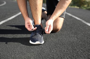 Güneşli bir sabahta ayakkabı bağcıklarını bağlayan sporcu, yakın plan.