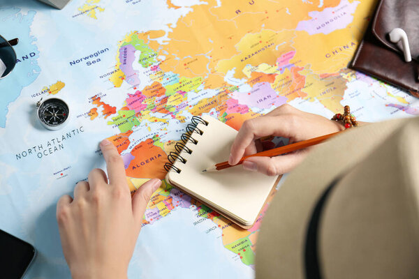 Woman using world map to plan trip at wooden table, closeup