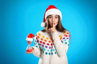 Açık mavi arka planda kum saati olan Noel Baba şapkalı bir kadın. Noel geri sayımı