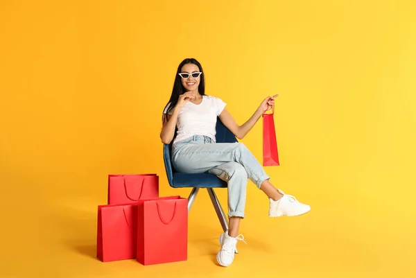 Hermosa Joven Con Bolsas Papel Sillón Sobre Fondo Amarillo —  Fotos de Stock