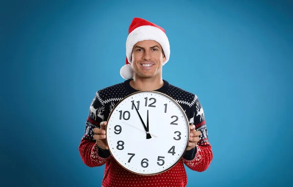 サンタの帽子の男は青い背景に時計をつけている クリスマスカウントダウン — ストック写真