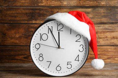 Noel Baba şapkalı saat, tahta arka planda gece yarısına beş dakika kaldığını gösteriyor. Yeni yıl geri sayımı