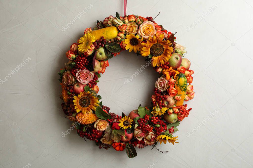 Beautiful autumnal wreath with flowers, berries and fruits hanging on light grey background. Space for text