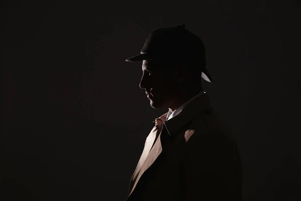 Old fashioned detective in hat on dark background. Space for text