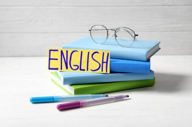 Kelime ENGLISH, kitaplar, gözlük ve keçeli kalemler beyaz ahşap masa üzerinde