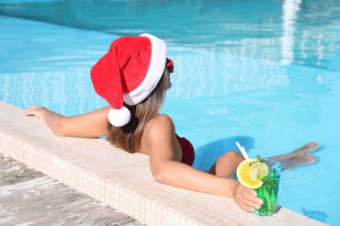 Yüzme havuzunda Noel Baba şapkası takan genç bir kadın. Noel tatili