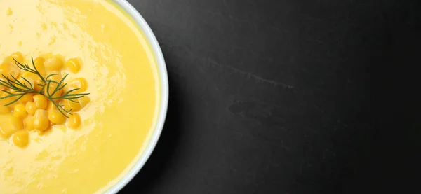 Delicious creamy corn soup on black table, top view