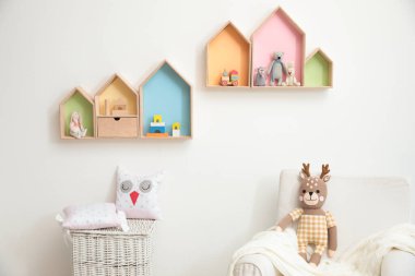 Ev şekilli rafları ve rahat koltuğu olan şık bir bebek odası iç tasarımı.